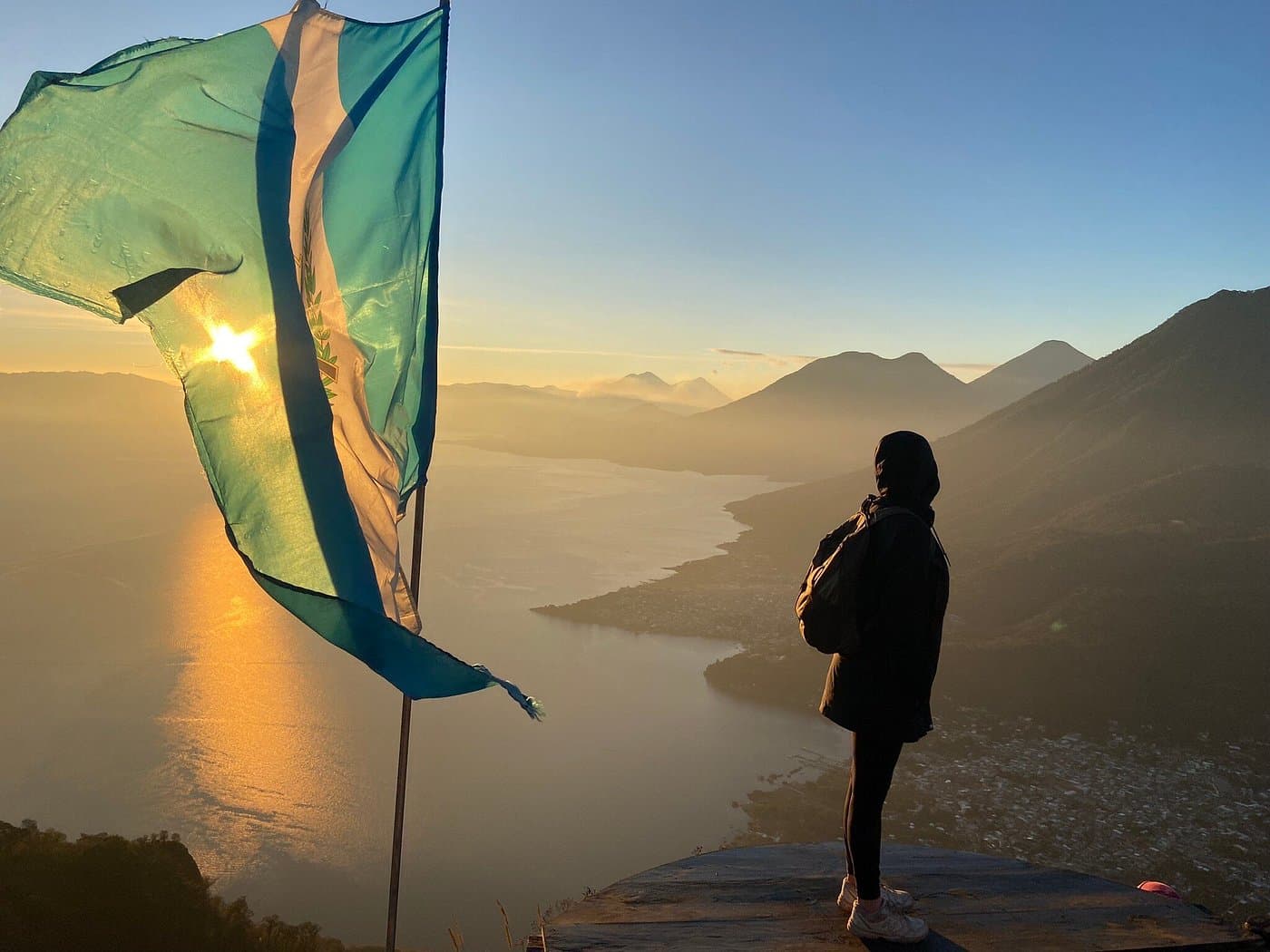 A Guatemalan flag backlit by a low sun on the Mayan Face ridge of the Indian Nose, with Lake Atitlán and its volcanoes below
