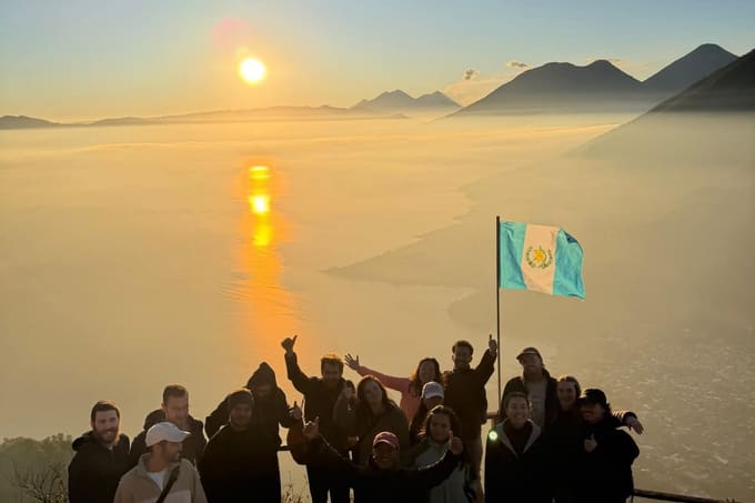 A tour group at the Rostro Maya summit with a Guatemalan flag, above Lake Atitlán